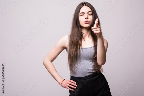 Happy pretty young woman standing and pointing at camera over gray background