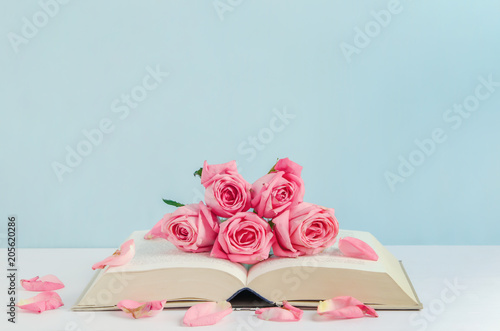 Vintage pink rose flowers with book on white and blue wooden background