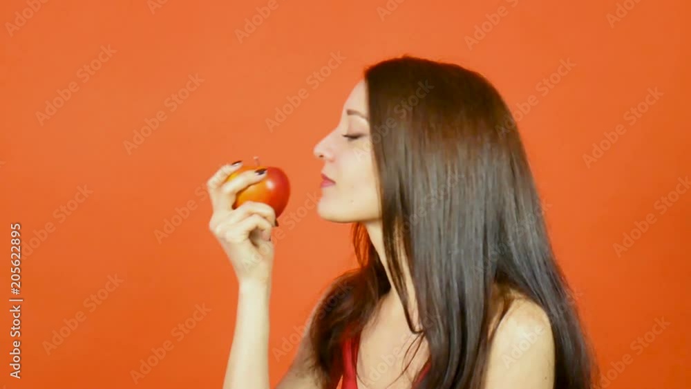 Smiling Woman with Healthy Teeth Eating Red Apple on Orange Background in Studio. Dieting Concept. Vegetarian Food. Smiling Woman with Healthy Teeth Eating Red Apple on Orange Background in Studio. Dieting Concept. Vegetarian Food.