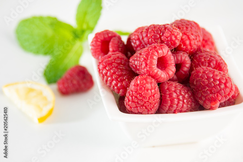 Raspberries with mint and lemon on white background.