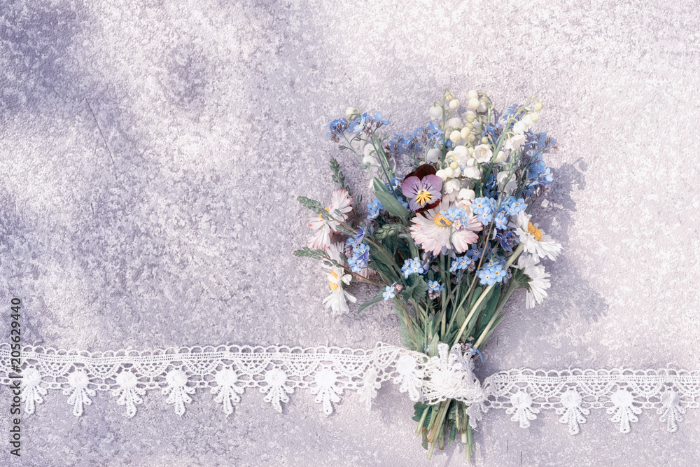Obraz premium forget me not, lily of the valley and wild flowers bouquet laying on an old rustic silver table in the lace frame with copy space for your greeting text.