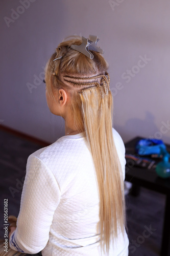 hair extensions, truss sewing, Hollywood build-up with pigtail, hair extensions in the blond beauty salon, hair sewn with threads and a needle, the process of execution, close-up on a light background