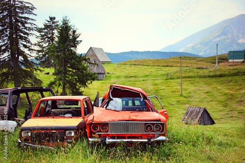 Four broken vehicles parked at the roadside on a green meadow in the background are meadows mountains and old wooden huts to see