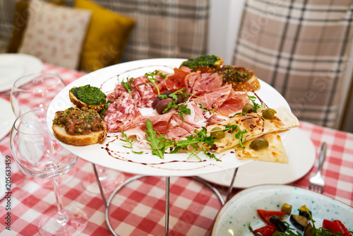 Meat antipasto platter on dinner table. Cold meat plate with prosciutto, salami, ham, bacon, sandwiches and olives on white plate, copy space. Italian prosciutto crudo or jamon with arugula. Raw ham