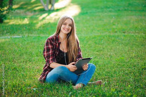 Young woman using tablet outdoor sitting on grass, smiling. © nagaets