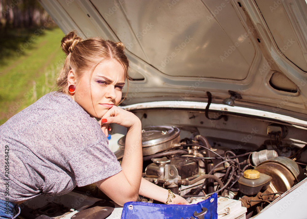 Beautiful young woman repairing an old car. The woman is upset because