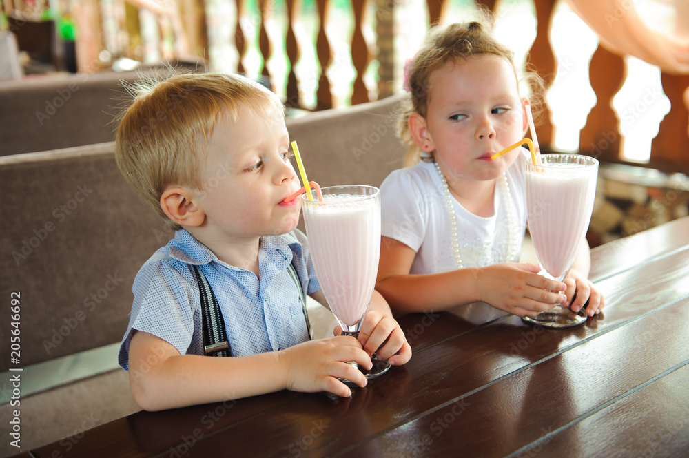 Little boy and girl drinking milkshakes in a cafe outdoors.