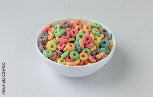 Dry sugar coated fruity flavored cereal in a bowl atop a white counter top.