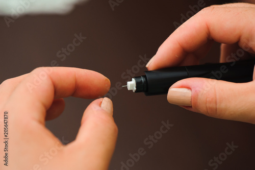Woman taking blood sample with lancet pen on wooden background. Diabetes concept.