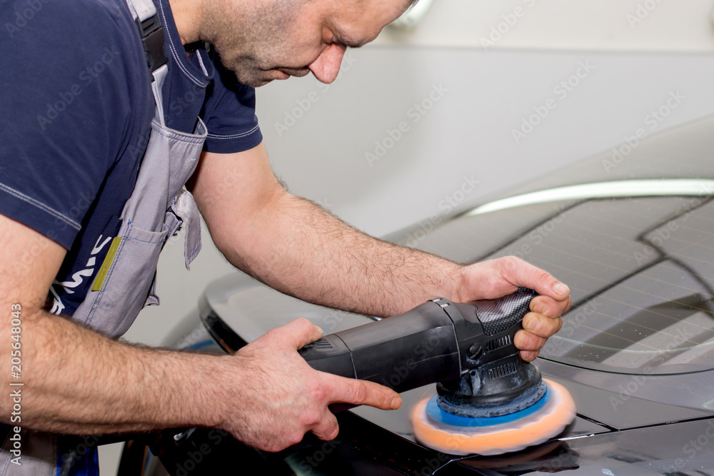 A man polishes a black car with a polisher A man polishes a black car with a polisher