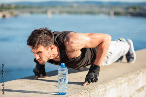 Determined young man doing two finger push-ups by the river. Exercising in urban environment