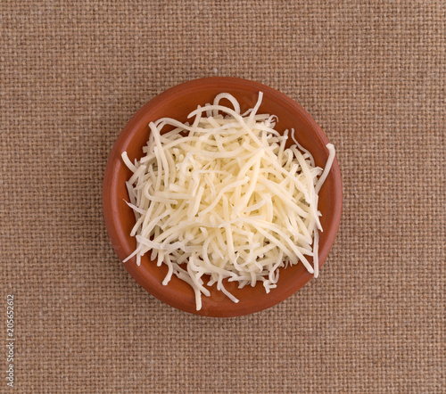 Top view of sharp white cheddar cheese in a small bowl on a brown tablecloth.