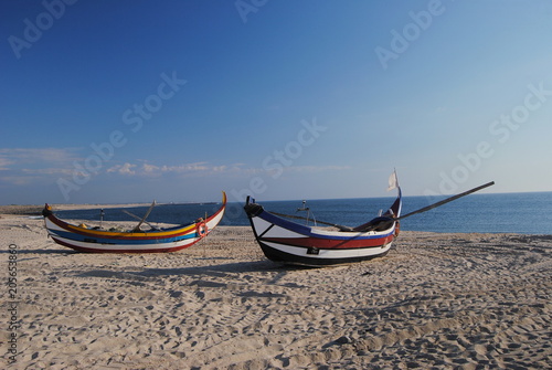 Barcos de pesca parados na areia da praia, pintados ás riscas amarela,azuis e vermelhas, com remos
