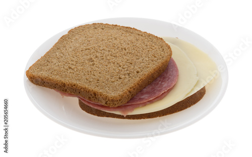 Genoa salami and provolone cheese wheat bread sandwich on a plate isolated on a white background.