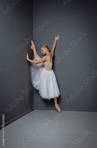 Young diligent dancer stretching her lag in the corner.