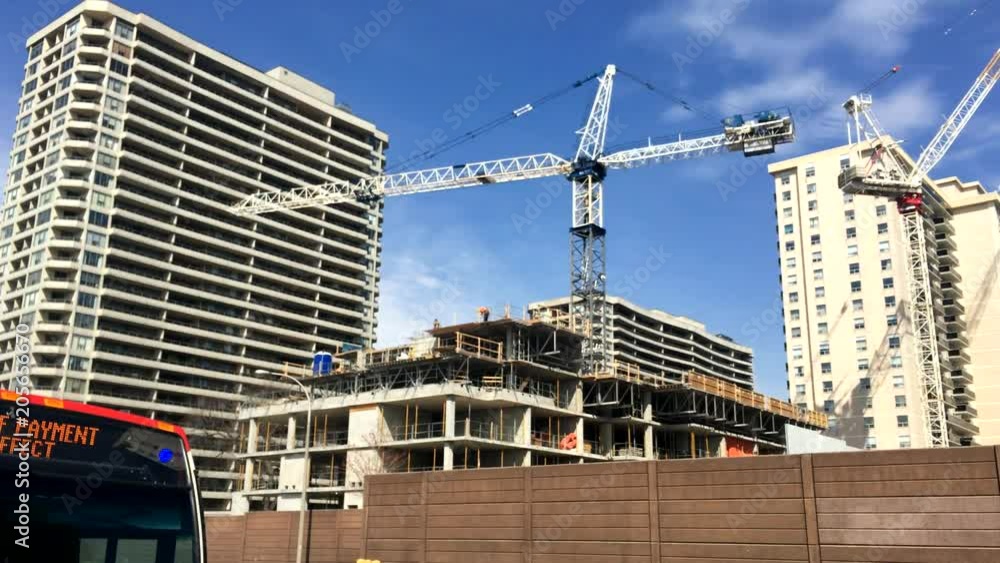 Tower crane operation in city next to a tall building, as a public bus passes by Tower crane operation in city next to a tall building, as a public bus passes by