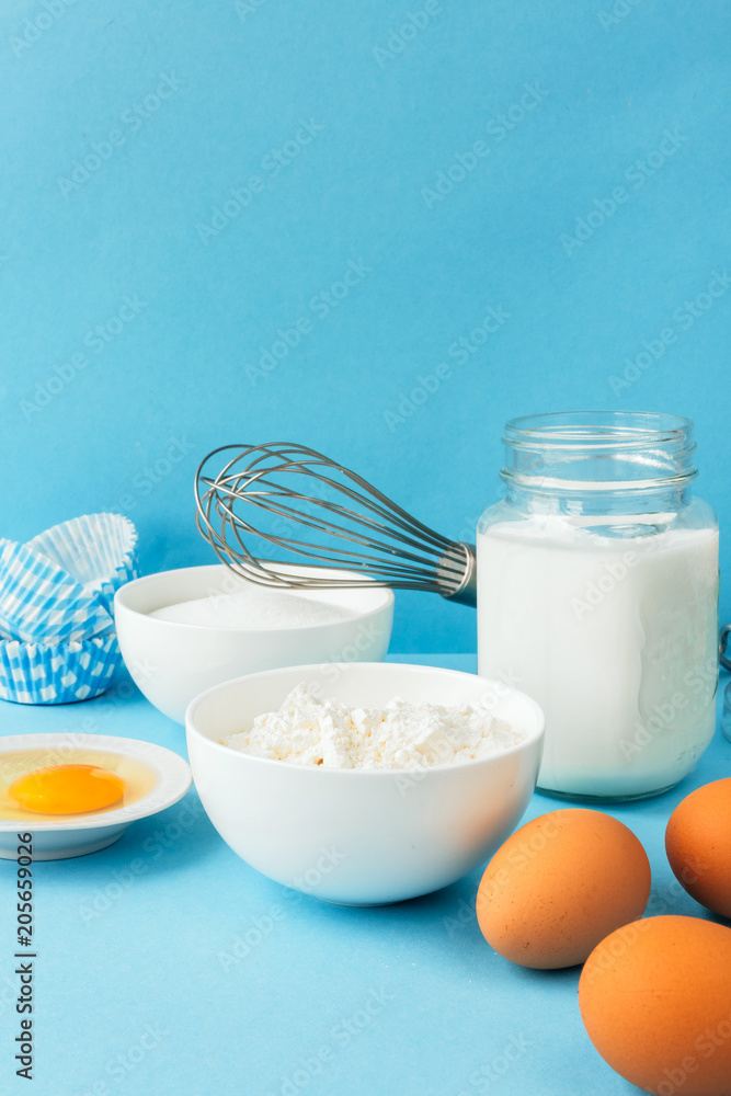 Eggs of chicken, flour in a bowl, sugar, milk in a glass jar whisk ingredient for cooking a bake on a blue background with copy space Eggs of chicken, flour in a bowl, sugar, milk in a glass jar whisk ingredient for cooking a bake on a blue background with copy space
