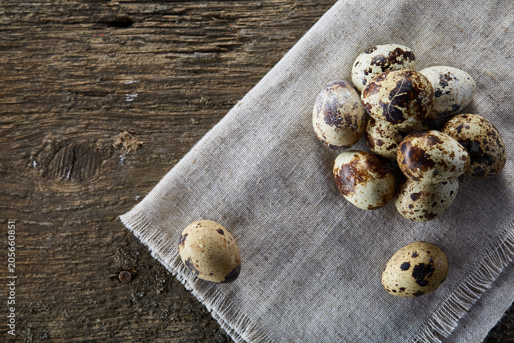 Quail eggs arranged in pyramid on a napkin with boxwood branches over a wooden table, close-up, selective focus.