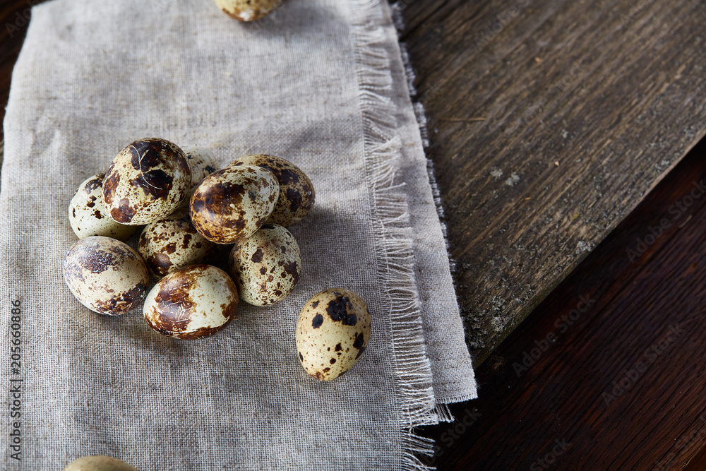 Quail eggs arranged in pyramid on a napkin with boxwood branches over a wooden table, close-up, selective focus. Quail eggs arranged in pyramid on a napkin with boxwood branches over a wooden table, close-up, selective focus.