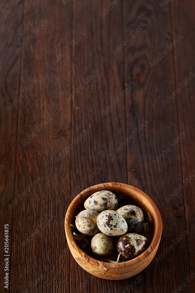 Fresh quail eggs in a wooden bowl on a dark wooden background, top view, close-up Fresh quail eggs in a wooden bowl on a dark wooden background, top view, close-up