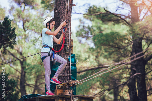 Obraz na plátne Happy school girl enjoying activity in a climbing adventure park on a summer day