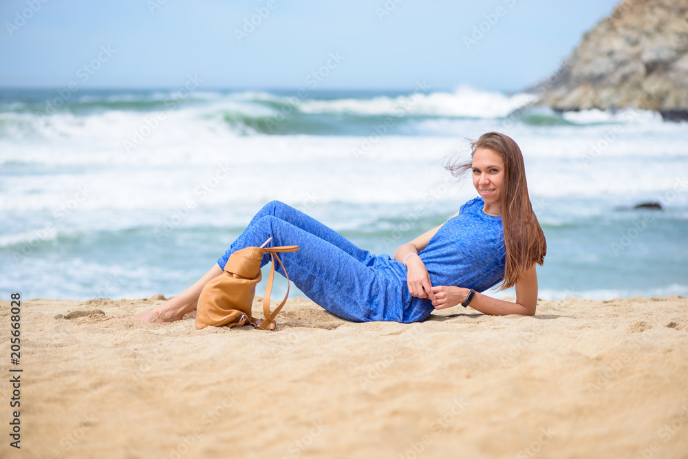 Beautiful young girl relaxing on the beach on vacation her bag nearby