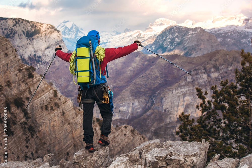 Young mountaineer standing with backpack on top of a mountain and enjoying the view