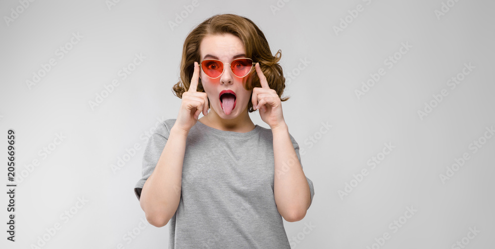 Charming young girl in a gray T-shirt on a gray background. Happy girl in red glasses. The girl adjusts glasses Charming young girl in a gray T-shirt on a gray background. Happy girl in red glasses. The girl adjusts glasses
