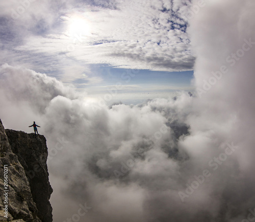 girl with hands up standing on a cliff in clouds