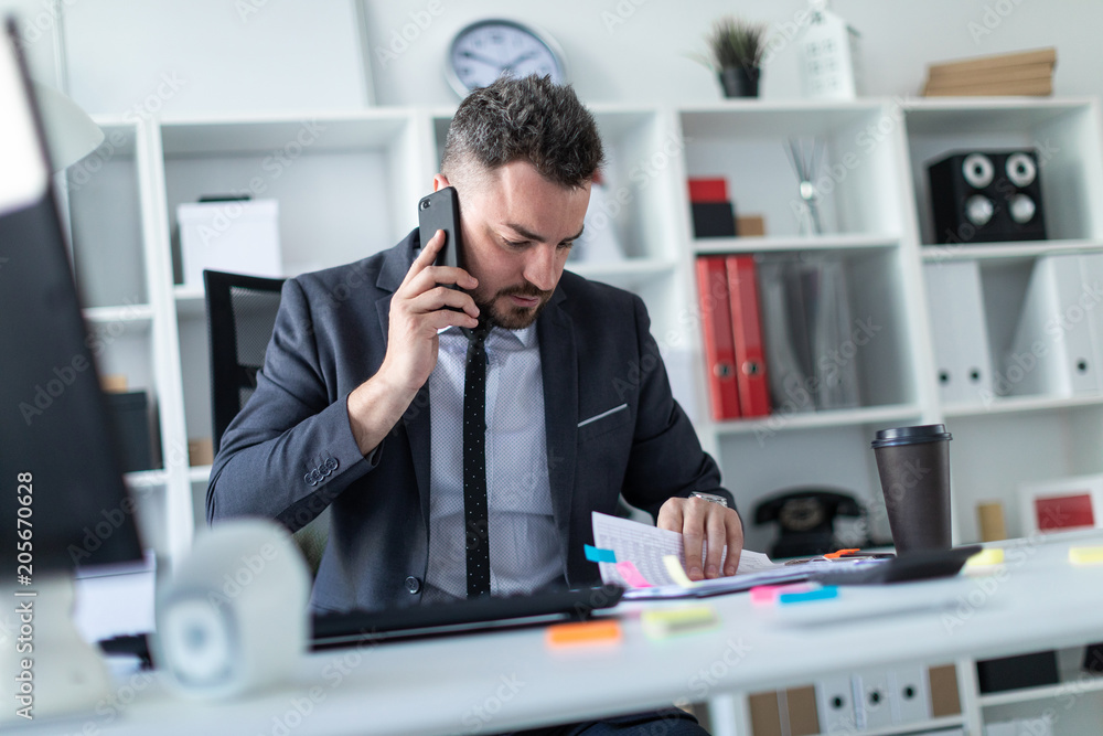 A man is sitting in the office at the table, talking on the phone and flipping through documents. A man is sitting in the office at the table, talking on the phone and flipping through documents.