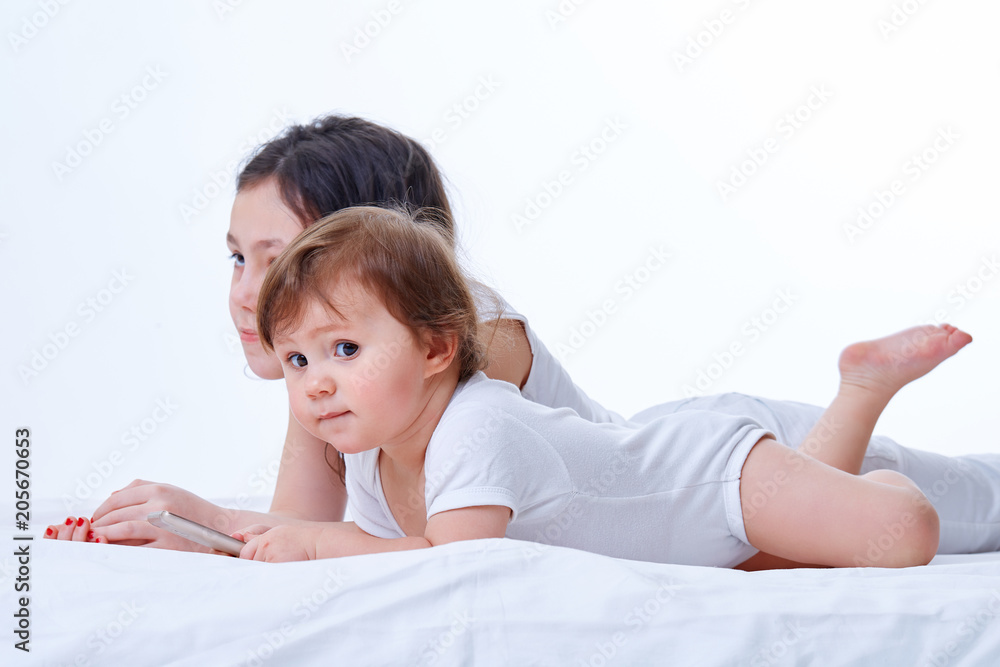 Two sister playing together in games on the smartphone in white studio background. Two sister playing together in games on the smartphone in white studio background.