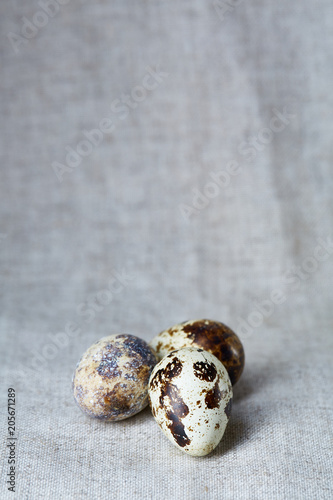 Fototapeta Naklejka Na Ścianę i Meble -  Group of three quail eggs on a homespun tablecloth, top view, close-up, selective focus, copy space, backlight.