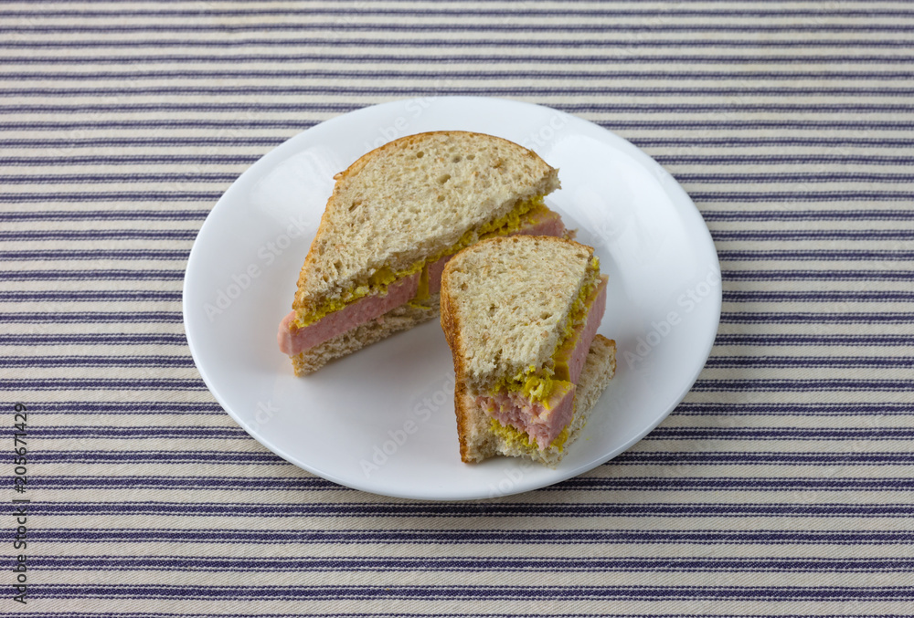 Pressed pork canned meat sandwich on wheat bread on a white plate atop a blue striped tablecloth. Pressed pork canned meat sandwich on wheat bread on a white plate atop a blue striped tablecloth.