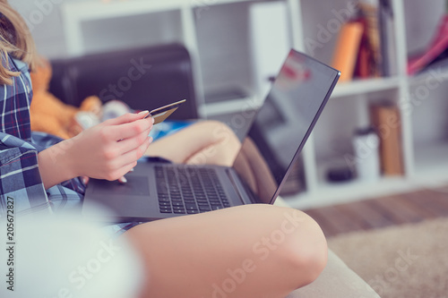 Woman's hands holding a credit card and using laptop for online shopping. Girl shopping online sitting on the couch at home.