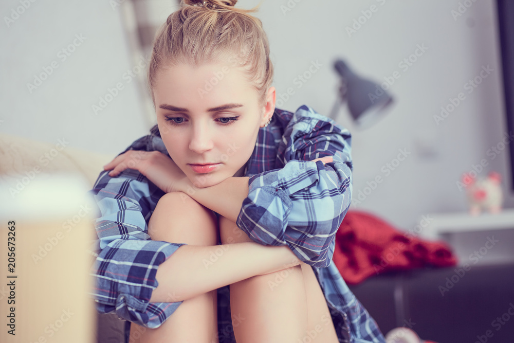 Naklejka premium Unhappy lonely depressed teenage girl at home, she is sitting on the couch and propped her head with his feet. Depression of adolescence concept.