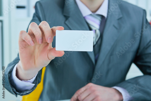 Businessman in grey suit and a pink shirt shows business card with copy space, shallow dept of field.