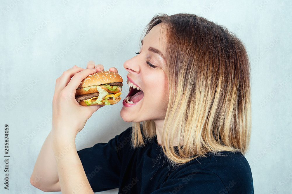 young and attractive blonde woman in black T-shirt and measuring tape eating a high-calorie burger. concept of harmful fast food and diet young and attractive blonde woman in black T-shirt and measuring tape eating a high-calorie burger. concept of harmful fast food and diet
