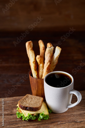 Breakfast table with sandwich and black coffee on rustic wooden background, close-up, selective focus