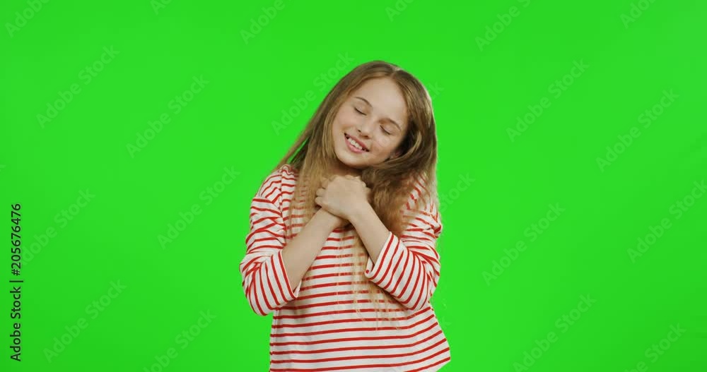 Blond pretty small girl with long hair doing gesture like she hugging somebody while standing on the green screen background. Green screen. Blond pretty small girl with long hair doing gesture like she hugging somebody while standing on the green screen background. Green screen.