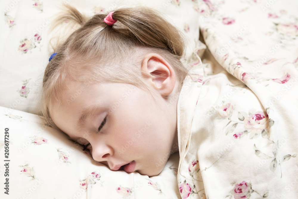 Little beautiful girl with a tail on her head asleep on a pillow, covered with a blanket, close-up