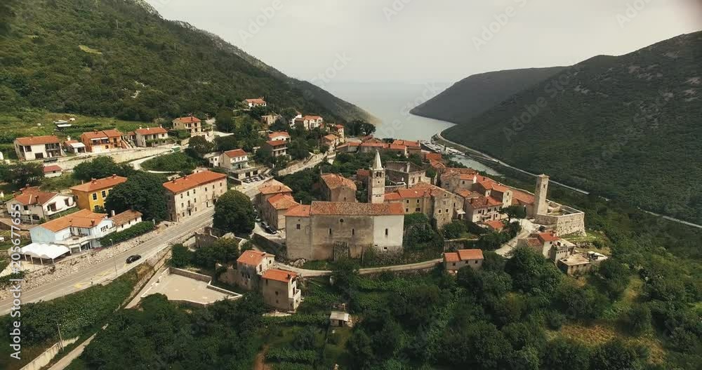 wide aerial shot of a croatian mountain village at cloudy weather with a beautiful landscape and a tourist ship in the background. camera moves backwards and ends in a super wide shot. wide aerial shot of a croatian mountain village at cloudy weather with a beautiful landscape and a tourist ship in the background. camera moves backwards and ends in a super wide shot.