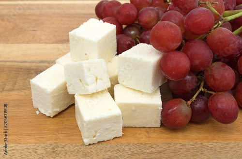 Feta cheese chunks with fresh grapes on a wood cheese board side view.