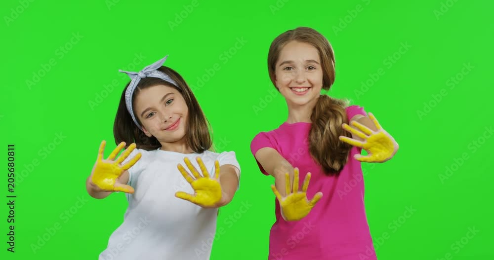 Funny teen girls in the T-shirts and with long hair posing to the camera with palms of the hands in yellow paint. Green screen. Chroma key. Funny teen girls in the T-shirts and with long hair posing to the camera with palms of the hands in yellow paint. Green screen. Chroma key.