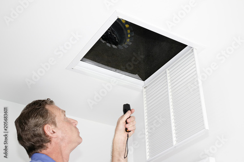 Man Inspecting Air Intake Duct
Male looking up into a ceiling air intake duct with a flashlight checking for maintenance. Man with a flashlight examining with a square opening of a home HVAC system