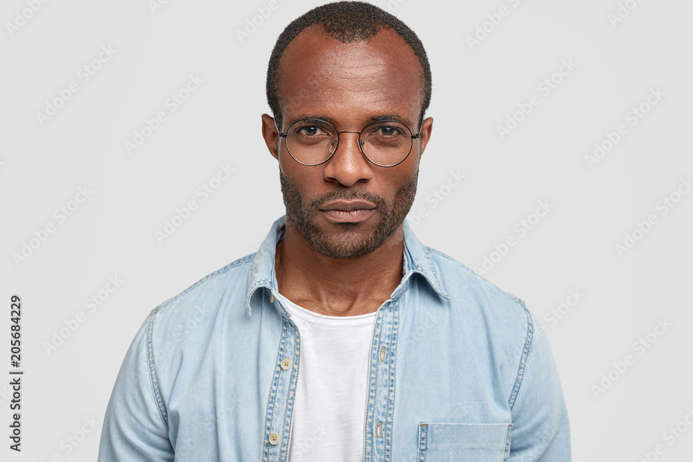 Headshot of good looking strict mysterious dark skinned male with stubble, wears denim shirt, looks scrupulously and seriously at camera, tries to understand what interlocutor is telling him Headshot of good looking strict mysterious dark skinned male with stubble, wears denim shirt, looks scrupulously and seriously at camera, tries to understand what interlocutor is telling him