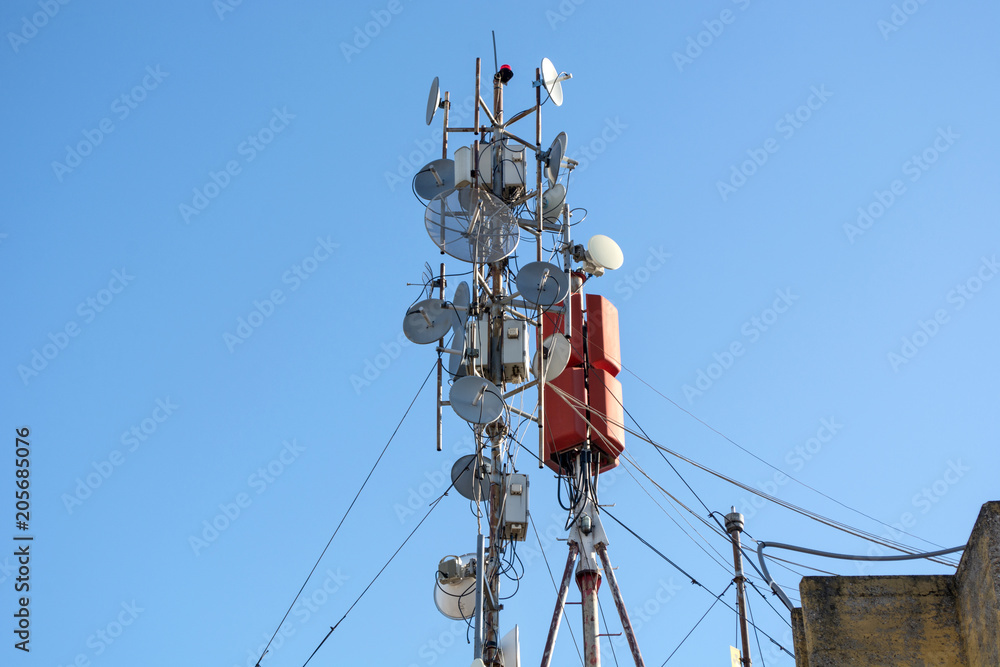 Lots antennas of wireless network, telecommunication and satellite dishes on a building roof. Panel antennas, fiber, optic and power cables of outdoor equipment of basic station. Lots antennas of wireless network, telecommunication and satellite dishes on a building roof. Panel antennas, fiber, optic and power cables of outdoor equipment of basic station.