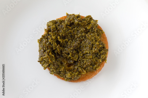 Chopped parsley spread on a cracker atop a white plate.