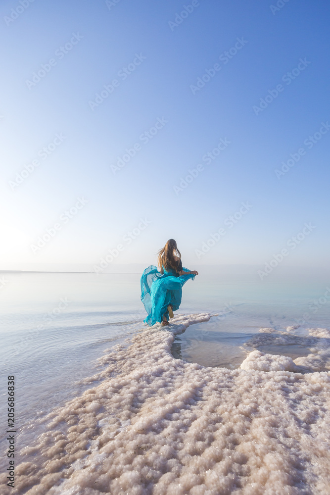 Blonde young woman in a blue dress on the shore of the dead sea. Jordan