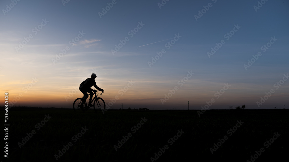 Silhouette of cyclist in motion on the background of beautiful sunset. Male ride bicycle in sun set. Silhouette of man biker ride a bike on sunsets sky on a field. Healthy Lifestyle. Sport.