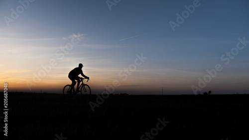 Silhouette of cyclist in motion on the background of beautiful sunset. Male ride bicycle in sun set. Silhouette of man biker ride a bike on sunsets sky on a field. Healthy Lifestyle. Sport.